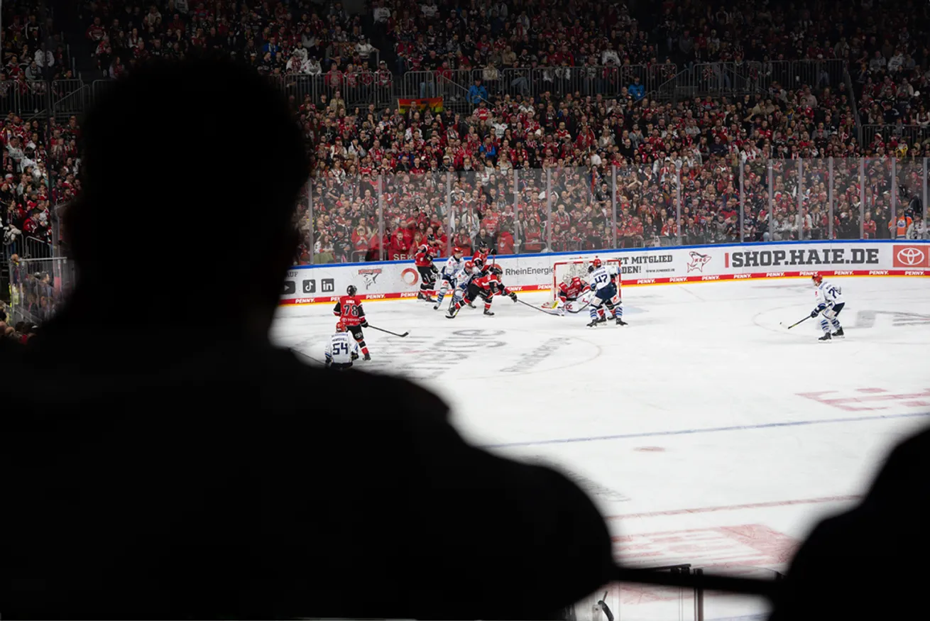 From a spectator's viewpoint, the image shows an ice hockey game with players in red and blue jerseys in front of a large crowd.