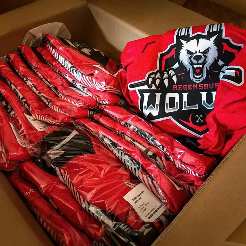 A box filled with several plastic-wrapped red sports jerseys, including a visible jersey featuring a wolf logo and the text 'Regensburg WOLV'.