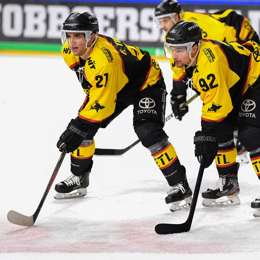 Two ice hockey players in yellow and black jerseys are on the ice.