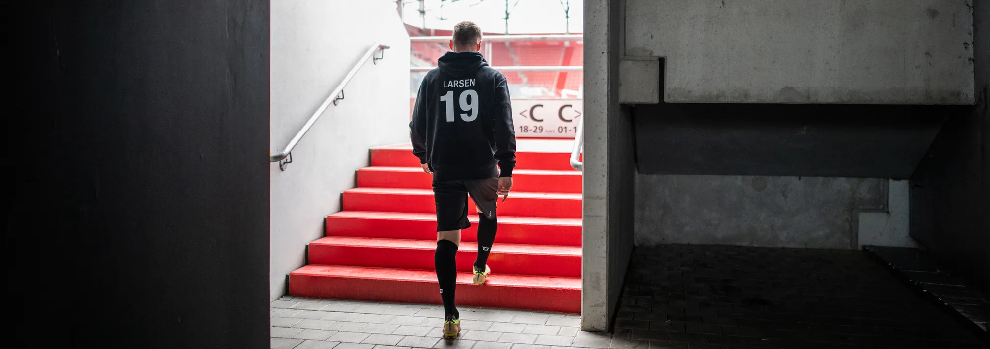 An athlete walks down the stairs in a sports outfit, heading towards the field.