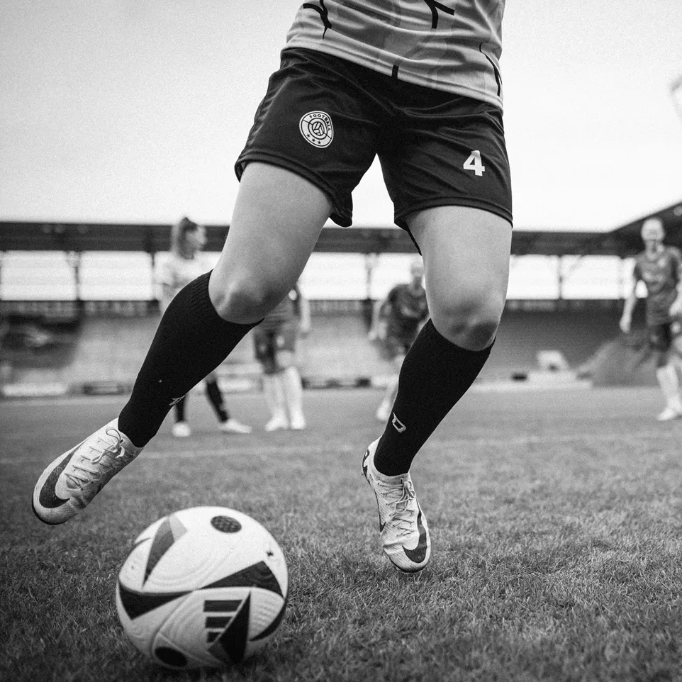 A player in shorts and socks dribbling a soccer ball on a grassy field.