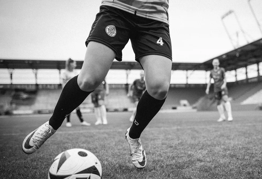 A female player in short soccer shorts and long socks is dribbling a ball on the field.