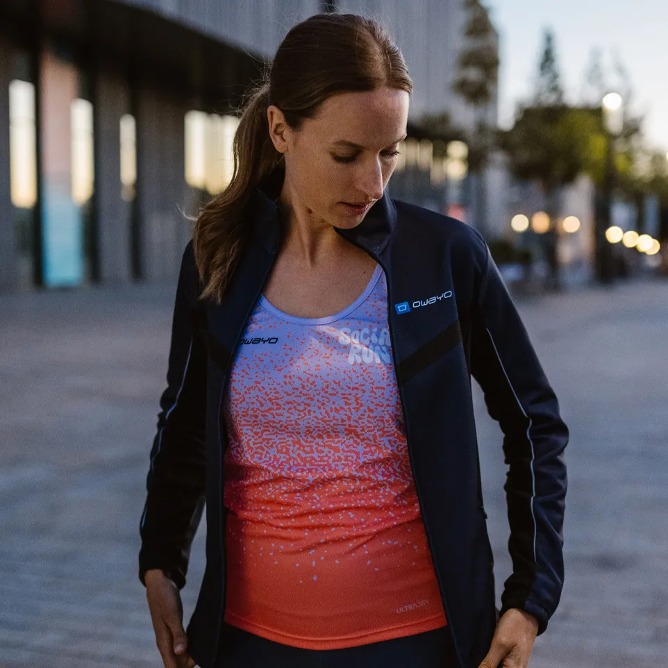 A woman is wearing a sporty jacket and a colorful sleeveless top with a modern design while standing on an urban street.