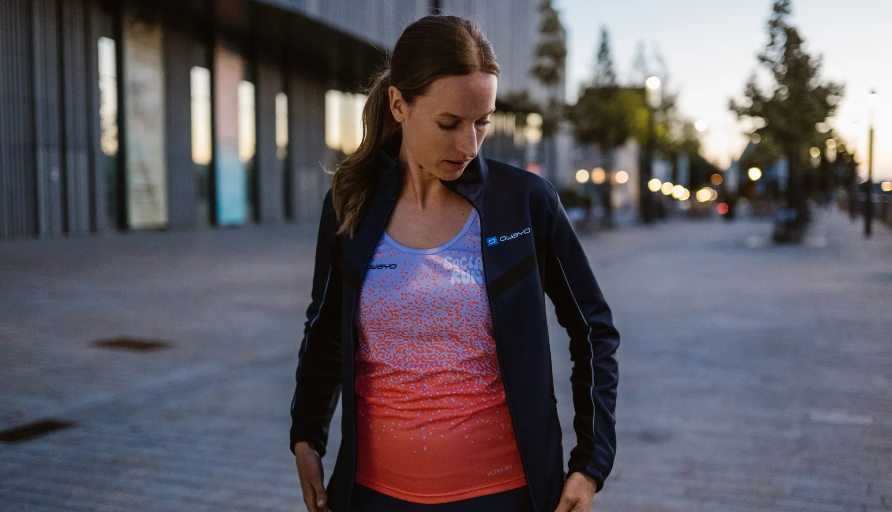A woman in a sporty outfit featuring a black jacket and a colorful, graphic tank top, standing on a sidewalk.