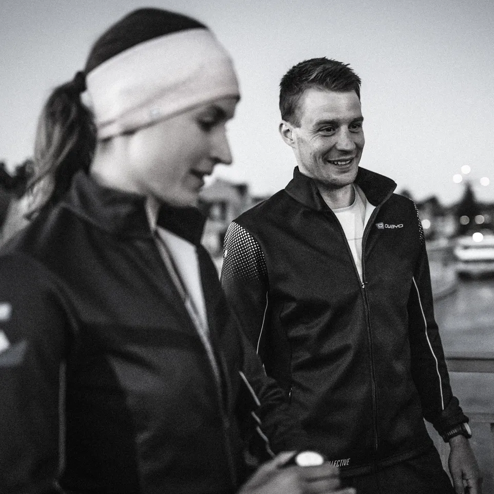 Two athletes in modern black jackets stand outdoors, smiling and ready for training.