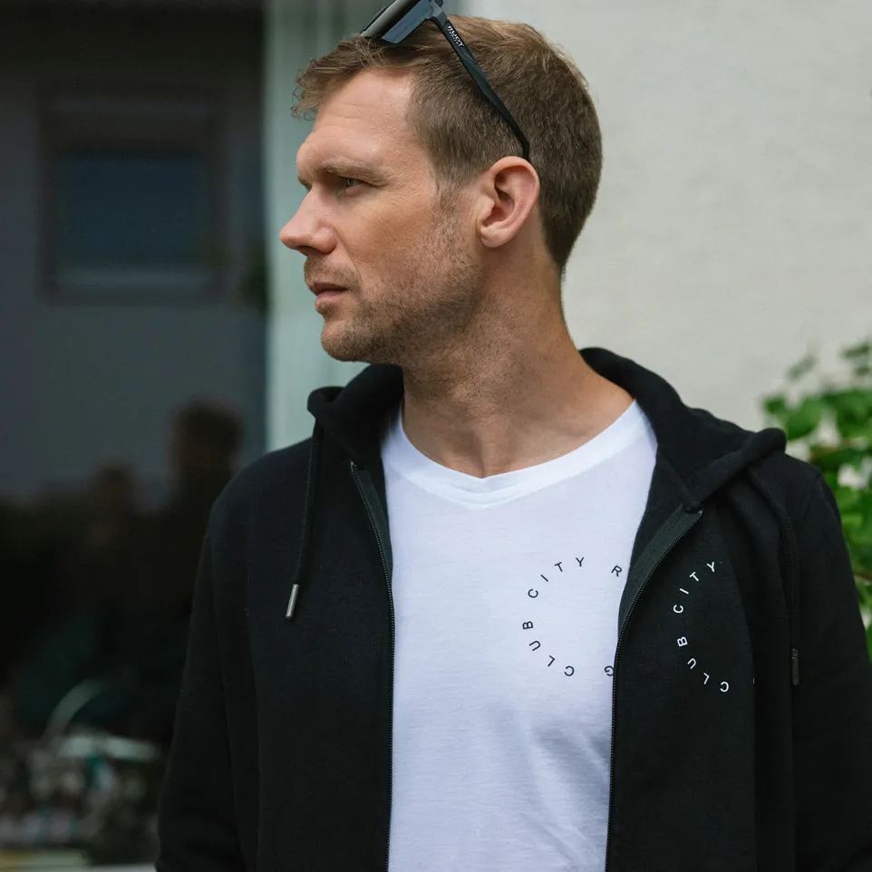 A man is wearing a black hoodie over a white t-shirt with a circular print.