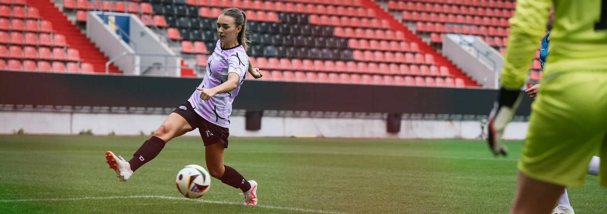 A female player in a purple soccer jersey is kicking the ball on a grass field.