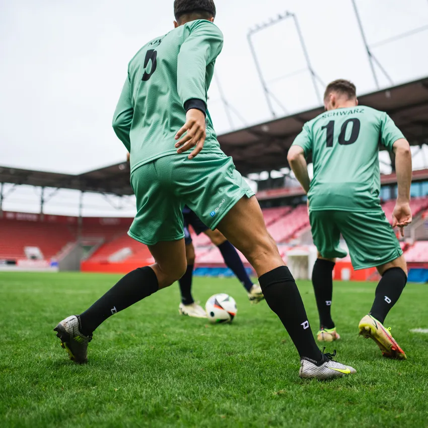 Two soccer players in green jerseys and black socks playing on a grass field with a ball.