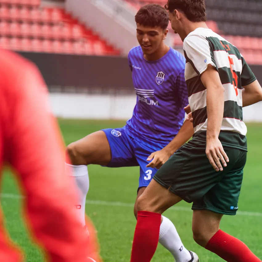 Two soccer players in action on the field, one wearing a blue jersey and the other in a green and red striped jersey.