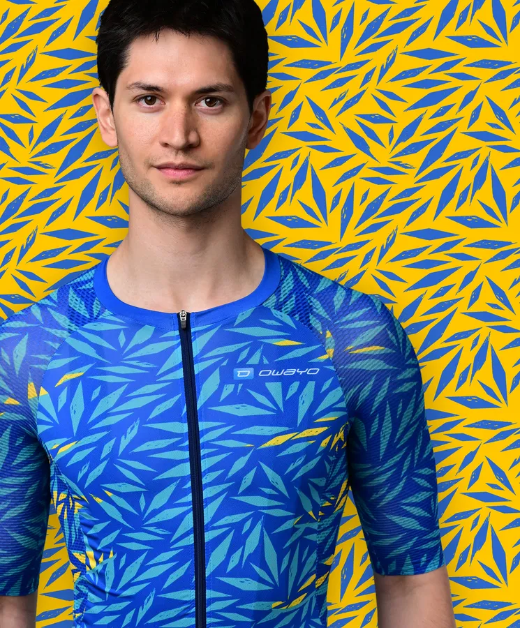 A man wears a blue, short-sleeved sport jersey with a blue and yellow leaf pattern resembling a tropical plant, against a yellow background with blue leaf patterns.
