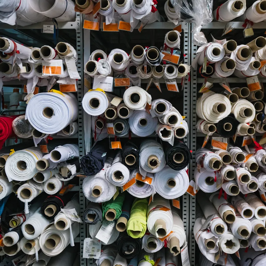 Shelves filled with rolls of fabric in various colors and sizes, used for manufacturing sportswear.